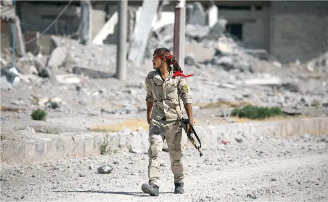  ??  ?? A Syrian Democratic Forces fighter walks along a damaged building in Raqqa’s Al-Sanaa industrial neighborho­od, on Wednesday. (Reuters)