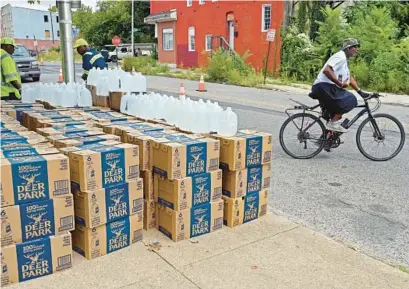  ?? KENNETH K. LAM/BALTIMORE SUN PHOTOS ?? A cyclist picks up bottled water from Baltimore’s Department of Public Works at West Lafayette and North Calhoun streets after E. coli was detected in the water in some locations in West Baltimore.