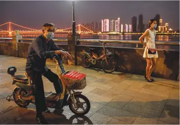  ?? (Hector Retamal/AFP via Getty Images) ?? A MAN and a woman wearing watch people dance in a park next to the Yangtze River in Wuhan, China, last week.