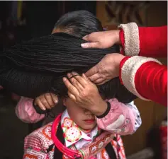  ??  ?? A girl (centre) getting her wig set prior to taking part in the annual flower festival or ‘Tiaohuajie’ in the village of Longjia in China’s Guizhou province. — AFP photo