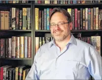  ?? AP PHOTO ?? Nathan Shafer, a life-long book collector, poses in front of his bookshelf in Arvada, Colo. Shafer said he feels there is no point to a backwards-facing bookshelf. “That’s not what books are for,” he said