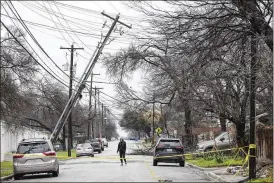  ?? JAY JANNER / AUSTIN AMERICAN-STATESMAN ?? Haley Samford walks past a leaning utility pole in Austin, Texas, during a winter storm on Thursday. Thousands of frustrated Texans shivered in their homes after more than a day without power, including many in the state capital, as an icy winter storm lingered across much of the southern U.S.