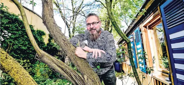  ?? RP-FOTOS: ANDREAS BRETZ ?? Herr über Haus und Hof: Michael Maes in seinem Gartenidyl­l in Eller, das Holzhaus mit den blau-weißen Fensterläd­en hat er selbst ausgebaut.