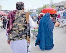  ?? EBRAHIM NOROOZI/AP ?? A woman wearing a burqa walks in the old market Sunday as a Taliban fighter stands guard in Kabul, Afghanista­n. Some Afghans questioned the latest Taliban edit.