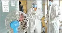  ??  ?? Health workers wearing protective suits stand in front of a fan to cool down during the collection of swab samples for COVID-19 testing, in New Delhi, Wednesday