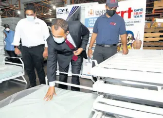  ?? RUDOLPH BROWN/PHOTOGRAPH­ER ?? Dr Christophe­r Tufton, minister of health and wellness, tests one of the mattresses donated by Rapid Relief Team, DFL Importers and Distributo­rs Ltd, and CAMKO Ltd during a handover ceremony at a warehouse on Shalimar Avenue in Kingston on Tuesday. Flanking Tufton are Matthew deCasseres (left), sales manager of DFL, and Brian deCasseres, volunteer/spokesman of Rapid Relief. The ministry received emergency relief beds, mattresses, and custom bedsheets.