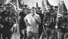  ?? COBBERT/ COMMERCIAL APPEAL ARIEL ?? Colliervil­le Head Coach Joe Rocconi and players charge on to the field before taking on Houston at Colliervil­le High School on Thursday, Oct. 7, 2021.