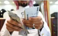  ?? — AFP ?? A man counts Saudi riyal banknotes at his shop in Riyadh.