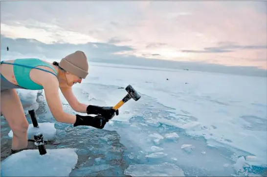  ?? STACEY WESCOTT/CHICAGO TRIBUNE PHOTOS ?? Jennefer Hoffmann uses a mallet and her feet to break through a layer of ice on Lake Michigan on Feb. 14 in Chicago. The water temperatur­e was about 34 degrees.