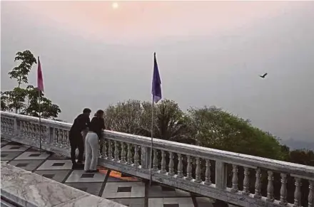  ?? AFP PIC ?? Tourists looking out at the horizon as high levels of air pollution obscure the view of Chiang Mai from atop Wat Phra That Doi Suthep temple yesterday. The city’s location, nestled between hills that trap toxic smog, has made the situation worse.