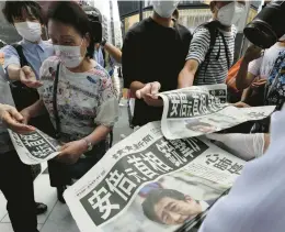  ?? EUGENE HOSHIKO/AP ?? Tokyo pedestrian­s snap up an extra edition Friday of the Yomiuri Shimbun newspaper covering the assassinat­ion of former Prime Minister Shinzo Abe earlier that day.