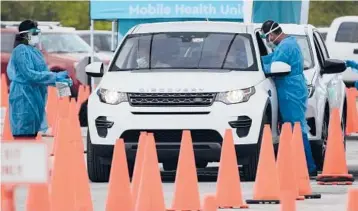  ?? REBECCA BLACKWELL/AP ?? Health care workers test motorists Monday at a dive-thru COVID-19 site at Zoo Miami in Florida.