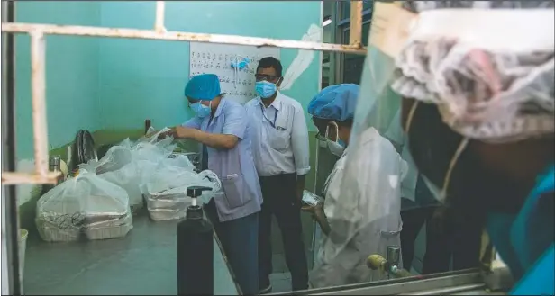  ?? (AP/Niranjan Shrestha) ?? Health workers receive free food packets as pharmacist Bikram Bhadel waits at Tribhuvan University Teaching Hospital, in Kathmandu, Nepal. The cafeteria and nearby cafes have closed because of lockdowns, leaving more than 200 staffers, patients and their families without food.