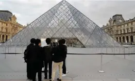  ?? SAMSON / AFP. THOMAS ?? Un grupo de turistas leía un rótulo en que se informa sobre el cierre temporal del gran museo francés debido a la emergencia por el covid-19.