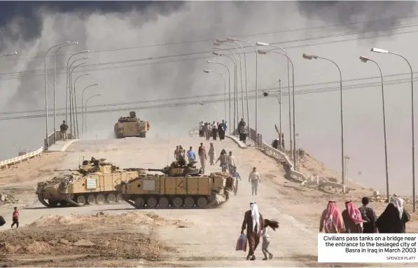  ?? SPENCER PLATT ?? Civilians pass tanks on a bridge near the entrance to the besieged city of Basra in Iraq in March 2003