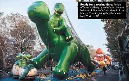  ?? — AP ?? Ready for a roaring time: Police officers walking by an inflated helium balloon of Sinclair’s Dino ahead of the Macy’s Thanksgivi­ng Day Parade in New York.