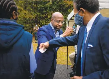  ?? Photog r aphs by Jason Armond Los Angeles Times ?? THE REV. Raphael Warnock, center, elbow bumps the Rev. Ralph Huling at a rally at St. James Missionary Baptist Church. “Everybody knows what’s at stake,” Huling says of the Jan. 5 Senate runoffs in Georgia.