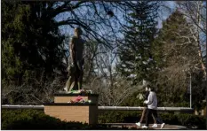  ?? NICK HAGEN — NEW YORK TIMES FILE ?? Students leave flowers under a statue on the Michigan State University campus after a mass shooting in February. The university warned that there had been an “uptick in the number of scams involving unlicensed Spartan Strong products” in the weeks since three students were killed in the campus shooting.