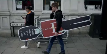  ?? (SIPA) ?? A man holding a sign shaped like a Royal guard, stating "don't let your guard down," as a reminder to keep on applying social distancing guidelines, Windsor, April 2021.