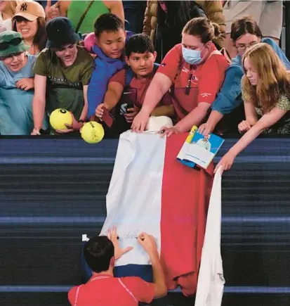  ?? AARON FAVILA/AP ?? Russia’s Daniil Medvedev autographs a Russian flag on Monday at the Australian Open. After another Russian flag was displayed during Ukrainian player Kateryna Baindl’s match, the tournament on Tuesday banned flags from Russia and Belarus over the invasion of Ukraine.