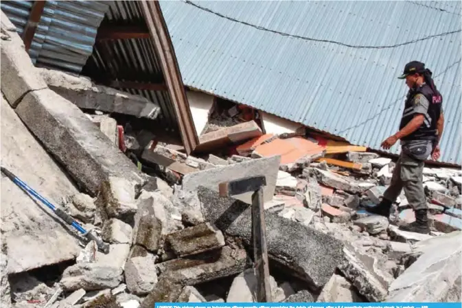  ??  ?? LOMBOK: This picture shows an Indonesian village security officer examining the debris of houses, after a 6.4 magnitude earthquake struck, in Lombok. — AFP