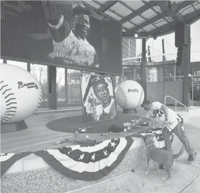  ?? JOHN BAZEMORE/AP ?? A man places flowers next to a portrait of Braves’ Hank Aaron on Friday outside Truist Park in Atlanta.