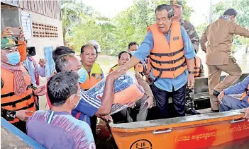  ??  ?? Cambodia’s prime minister Hun Sen (centre) offers aid to a flood survivor from a speedboat in Banteay Meanchey province.
