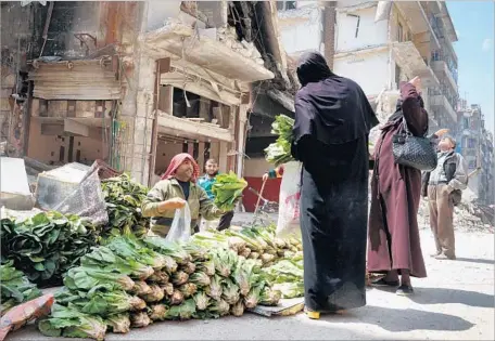  ?? Liliana Nieto del Rio For The Times ?? PRODUCE VENDOR Mohammed Abdullah, 42, helps customers from his stand on a rubble-strewn street in eastern Aleppo, where most neighborho­ods are still ghost towns. People look up at passing Syrian government fighter jets, more out of curiosity these days...