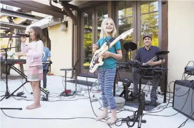  ?? Photos by Scott Strazzante / The Chronicle ?? Stella Goss plays the guitar as Reah Canada sings and teacher Mike Hoffman plays drums during a performanc­e of the kid band Good Stuff in the backyard of Google employee Lydia Mazzie’s home in Menlo Park.