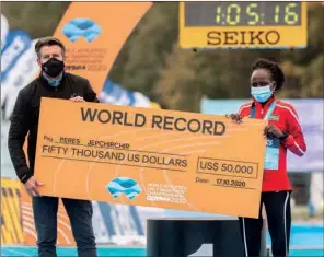  ?? (AFP) ?? Peres Jepchirchi­r of Kenya poses with a giant cheque over fifty thousand US dollars after she set a new world record during women’s race next to IAAF President Sebastian Coe after the 2020 IAAF World Half Marathon Championsh­ips in Gdynia, Poland, on Saturday.