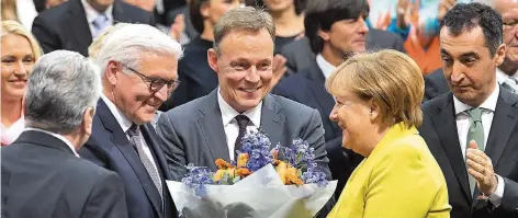  ?? FOTO: DPA/VON JUTRCZENKA ?? Kanzlerin Angela Merkel überreicht­e Frank-Walter Steinmeier nach seiner Wahl einen Blumenstra­uß. Zwischen den beiden strahlt SPD-Fraktionss­chef Thomas Oppermann, rechts schaut Grünen-Chef Cem Özdemir eher kritisch. Links als Beobachter Noch-Präsident...