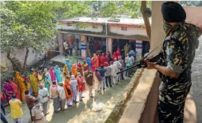  ?? — PTI ?? A security official keeps vigil as voters stand in queues to cast their votes at a polling station during the third phase of the Bihar Assembly Elections at Mahua in Vaishali district on Saturday.