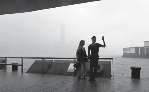  ??  ?? PENDUDUK sempat merakam swafoto di hadapan Pelabuhan Victoria ketika angin kuat dan hujan yang dibawa Pakhar membadai Hong Kong, semalam. — Gambar AFP