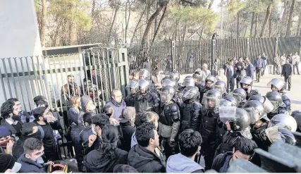  ??  ?? > Anti-riot police prevent university students joining other protesters demonstrat­ing in Tehran over Iran’s economy