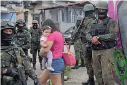  ??  ?? RIO DE JANEIRO: A woman carries her child as she walks past military police on patrol near the Vila Kennedy favela in Rio de Janeiro yesterday. —AFP