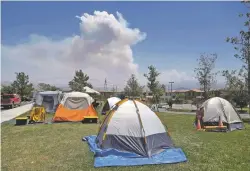 ?? NICK UT/THE ASSOCIATED PRESS ?? Dozens of tents for firefighte­rs cover a field at a firefighte­r operations base camp Tuesday that has been establishe­d at Golden Valley High School in Santa Clarita, Calif., as smoke from the Sand Fire looms.