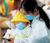  ??  ?? A mother and child in protective gear at Wuhan airport after lockdown was relaxed in April 2020