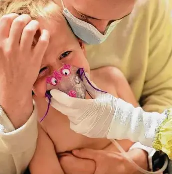  ?? Tribune News Service file photo ?? Meredith Legree of Lakeville, Minn., holds her son Andrew as respirator­y therapist Sirena Ortega places a mask on his face to help him to breathe easier as they wait for RSV test results.