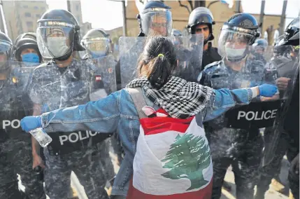  ??  ?? An anti-government protester confronts police during a protest against the deepening financial crisis in Beirut, Lebanon, on Tuesday. Hundreds of protesters in Lebanon's northern city of Tripoli set fire to two banks and hurled stones at soldiers.