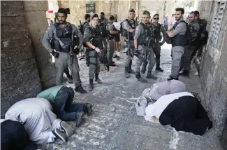  ?? — AP ?? JERUSALEM: Palestinia­ns pray as Israeli border police officers stand guard at Lion’s Gate in Jerusalem’s Old City yesterday.