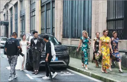  ?? GAO ERQIANG / CHINA DAILY ?? In a fleeting moment of cultural exchange, foreign women dressed in cheongsams pass a Chinese couple in Western-style suit and dress as they prepare for wedding photos on Dianchi Road in the Bund area of Shanghai on Sunday.