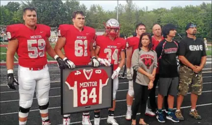  ?? JOHN KAMPF — THE NEWS-HERALD ?? The Mentor football team captains presented the family of the late Jacob Rago with a framed jersey prior to the Cardinals’ season-opener against St. Edward on Aug. 24. From left are Nick Samac (59), Ryan Jacoby (61), Brady Benz (34), Jean Rago, Danny Rago and Chris Rago. Behind the Rago family are Mentor captain Daniel Adams and Mentor coach Steve Trivisonno.