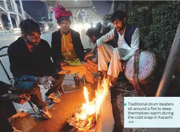  ?? APP ?? Traditiona­l drum beaters sit around a fire to keep themselves warm during the cold snap in Karachi.