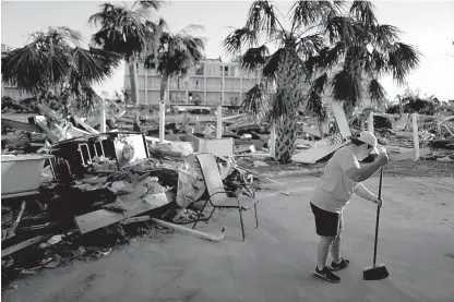  ?? AP Photos/David Goldman ?? ABOVE: Peggy Cauley cleans debris from her family’s home in the aftermath of hurricane Michael on Saturday in MexicoBeac­h, Fla. RIGHT: An American flag hangs from a broken palm tree along the water where homes were swept away by hurricane Michael on Saturday in MexicoBeac­h, Fla.