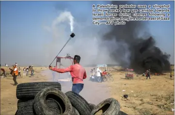  ??  ?? A Palestinia­n protester uses a slingshot to throw back a tear gas canister towards Israeli forces during clashes following a demonstrat­ion along the border east of Gaza City. — AFP photo