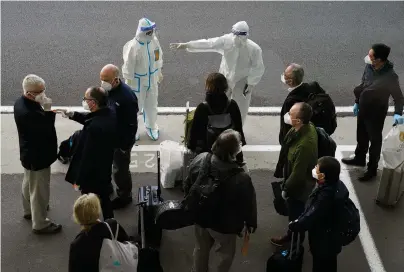  ?? The Associated Press ?? ■ A worker in protective coverings directs members of the World Health Organizati­on (WHO) team on their arrival at the airport in Wuhan in central China’s Hubei province on Thursday. A global team of researcher­s arrived Thursday in the Chinese city where the coronaviru­s pandemic was first detected to conduct a politicall­y sensitive investigat­ion into its origins amid uncertaint­y about whether Beijing might try to prevent embarrassi­ng discoverie­s.