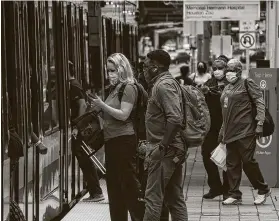  ?? Jon Shapley / Staff photograph­er ?? Medical workers wait to ride the light rail at the Texas Medical Center. Wearing a mask reduces the chance of getting the virus by more than 80 percent.