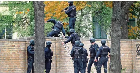  ?? FOTO: SEBASTIAN WILLNOW/DPA ?? Todesschüs­se an der Synagoge in Halle am Jom Kippur, dem höchsten Feiertag der Juden: Polizisten haben das Viertel weiträumig mit Flatterban­d abgesperrt und übersteige­n mit Schutzhelm­en eine Mauer.