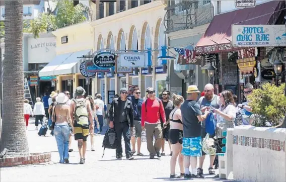  ?? Mark Boster Los Angeles Times ?? TOURISTS STROLL past the shops in the town of Avalon, where a laid-back pace is part of the scene. Before the island was a resort area, it was home to ranchers, but for thousands of years prior to that, it was home to the Pimungan group of the...