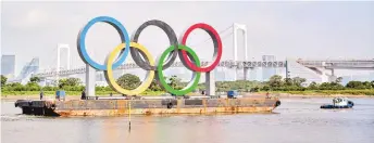  ?? — AFP photo ?? A large size Olympic rings symbol (W32.6m x H15.3m) is seen in front of Rainbow Bridge at Tokyo Waterfront in the waters of Odaiba Marine Park while being transferre­d back to the factory where it was manufactur­ed for a safety inspection and to receive maintenanc­e in this Aug 6 file photo.